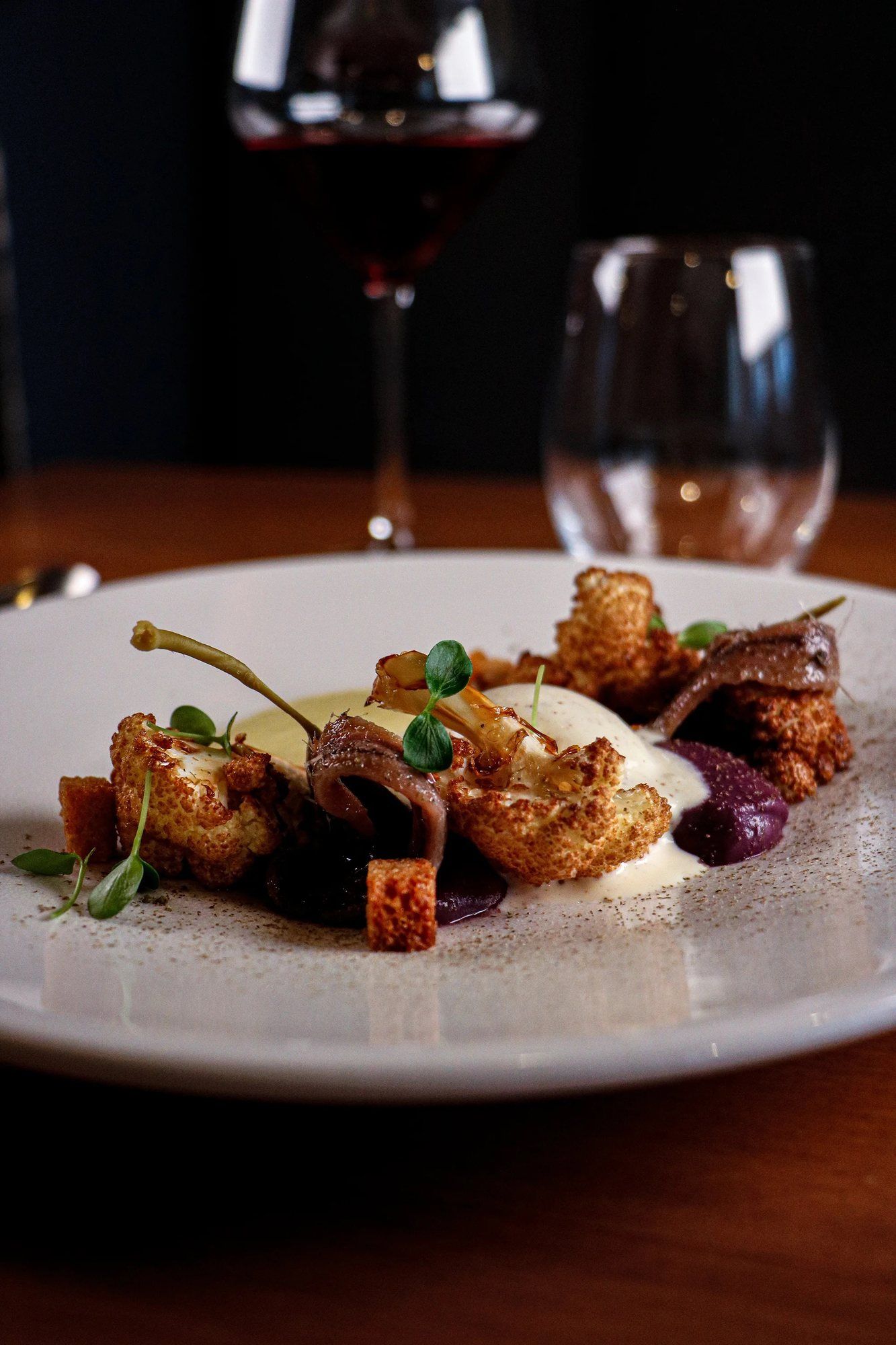 Une assiette dressée photographiée en salle, verres de vin en arrière-plan.