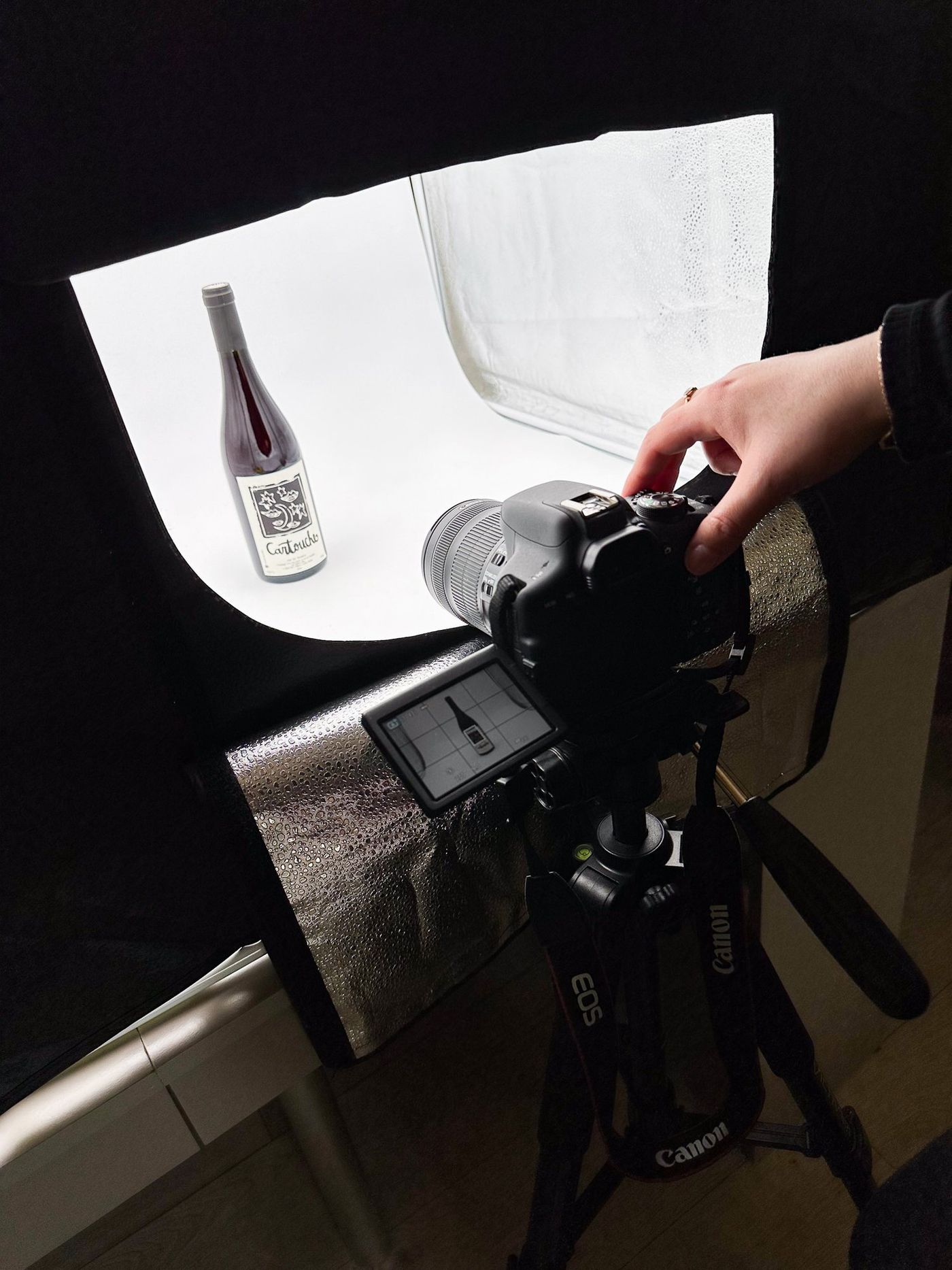 Une bouteille photographiée sous une boîte à lumière, appareil sur trépied.
