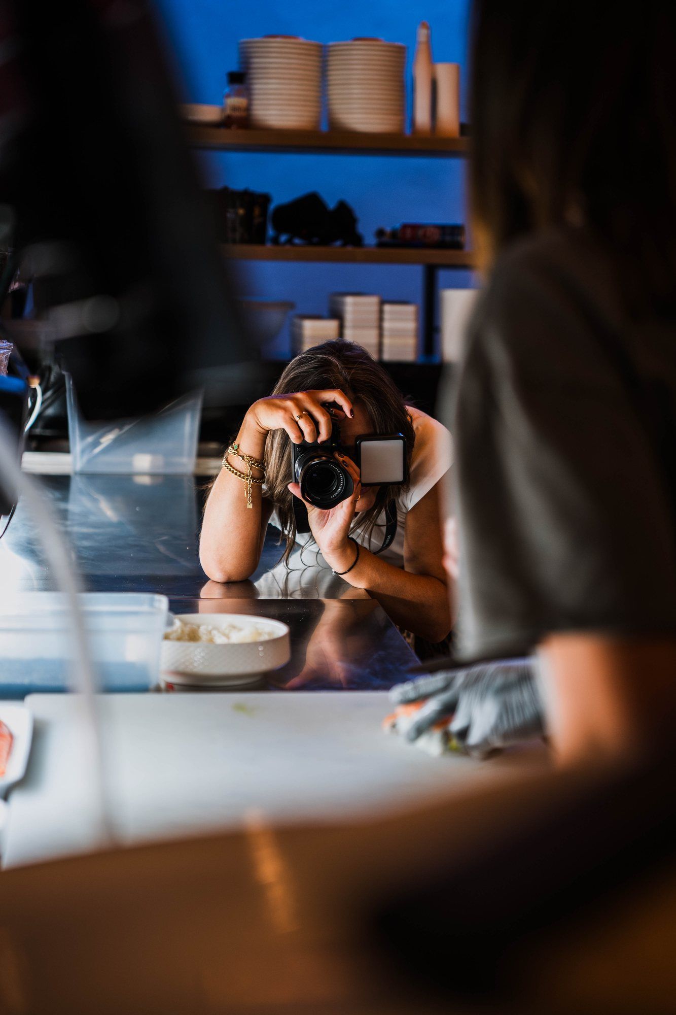 Une photographe de l’équipe cadre un plat posé sur le passe, en cuisine.